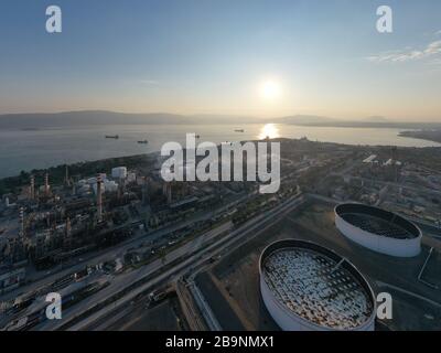 Vista aerea della pianta chimica al tramonto, raffinazione del petrolio, fumo, tubi, inquinamento ecologico, infezione dell'aria, costa del mare in Grecia, petroliere si aspettano Foto Stock