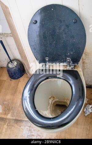 la toilette era molto sporca, con sedile e coperchio neri, molto calcare in una teglia asciugata. Calza scartata, spazzolina sporca e pareti e pavimento macchiati. Foto Stock