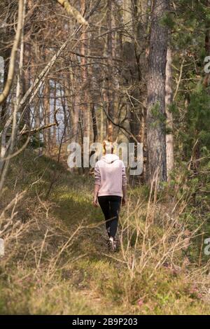 Vista posteriore di una donna sportiva attiva che ascolta la musica mentre corre nella foresta autunnale. Allenamento femminile all'aperto. Un'immagine sana dello stile di vita Foto Stock