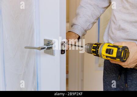 Un uomo che installa una serratura su una serratura di legno con un cacciavite Foto Stock