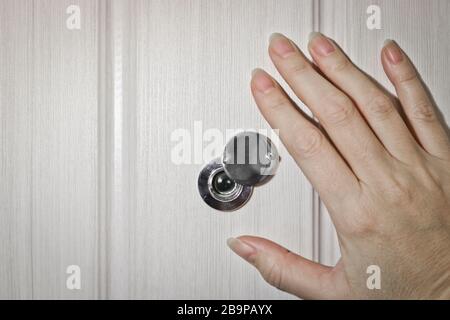 Una mano femmina apre la serranda sul peephole della porta anteriore. Il concetto di sicurezza e cautela. Foto Stock