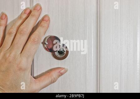 Una mano femmina apre la serranda sul peephole della porta anteriore. Il concetto di sicurezza e cautela. Foto Stock