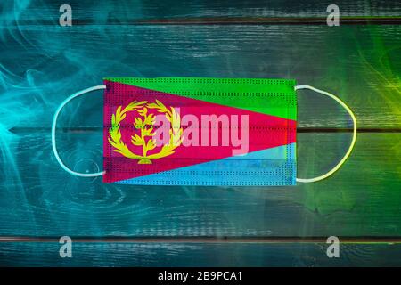 Maschera medica per la protezione contro le malattie trasmesse dall'aria, dipinta sulla bandiera nazionale della Guinea su sfondo nero con fumo blu-verde. Prote medico Foto Stock