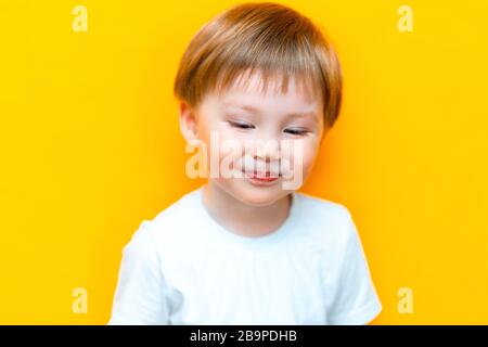 Piccolo bambino timido di tre anni isolato su sfondo giallo guardare verso il basso e sorridere Foto Stock