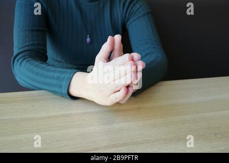 Palme piegate in preghiera. La ragazza si siede e tiene le mani davanti alle mani agganciate insieme. Foto Stock