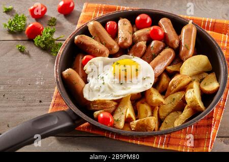 Salsicce e zeppe di patate da cocktail vengono servite con uova fritte in una padella, pronte per essere consumate Foto Stock