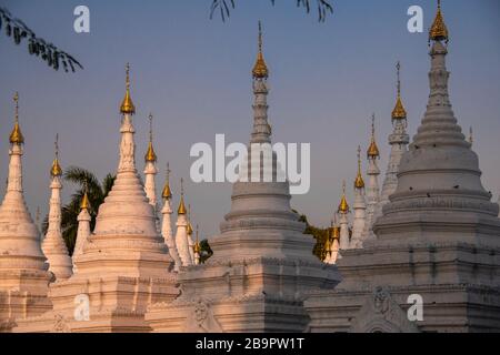 Sandamuni Pagoda, Mandalay, Myanmar. Stupa bianca con cime ornamentali in oro HTi (a forma di ombrello) contro un cielo al tramonto Foto Stock