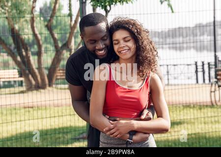 Attività all'aperto. Coppia africana in piedi in campo abbracciando sorridente felice Foto Stock