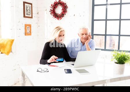 High Angle shot di shopping di coppia senior felice online. Donna anziana attraente che tiene la carta di banca nella sua mano mentre l'uomo anziano che siede dietro la loro l Foto Stock