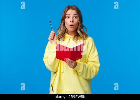 Ragazza che fa i compiti infine hanno un grande piano, fatto-up idea per la storia come la scrittura in rosso notebook, sollevare penna eureka gesto, guardando stupito fotocamera Foto Stock