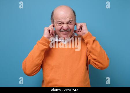 Uomo maturo che soffre di musica forte e dolore che cerca di tappi per orecchie Foto Stock