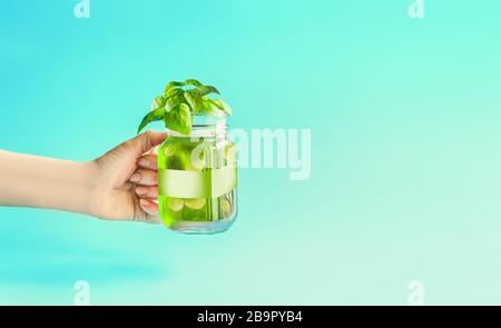 Bevanda estiva verde, limonata con cetrioli e fette di limone, aromatizzata con erbe in vaso Mason in donne mano a fondo di menta turchese. Summe Foto Stock