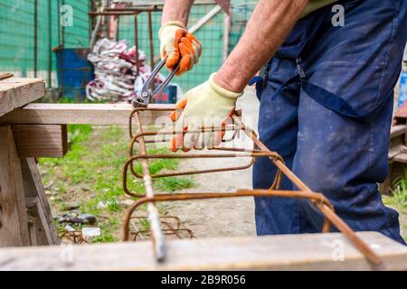 Lavoratore è la legatura rebar con filo servendosi di una pinza per fare un telaio di rinforzo per la trave di calcestruzzo. Foto Stock