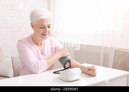 Signora anziana con ipertensione che misura la pressione sanguigna lei stessa Foto Stock