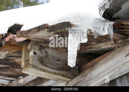 Ghiaccio rotto e ghiaccio fondente su un tetto coperto di neve come simbolo di fine inverno e prossima primavera Foto Stock
