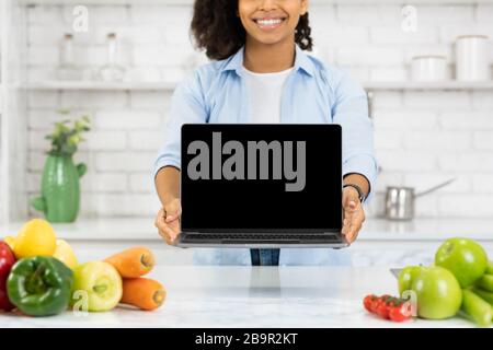 Irriconoscibile ragazza nera che tiene il laptop in cucina Foto Stock