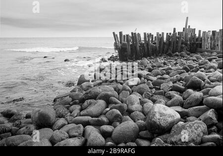 Castle Haven, Reeth Bay, Isola di Wight, Inghilterra, Regno Unito: Guardando fuori sul canale inglese in una giornata tranquilla, con massi e una vecchia frangiflutti in primo piano. Fotografia a pellicola in bianco e nero Foto Stock