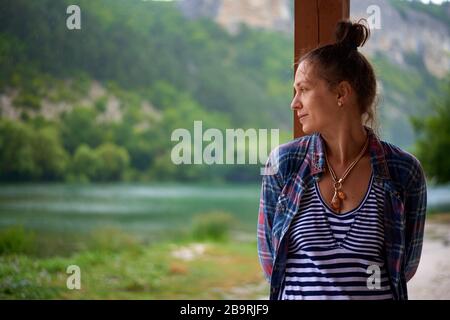 Bella felice donna sorridente bagnato durante la giornata piovosa soggiorno vicino al lago in montagna. Concetto di stile di vita. Foto Stock