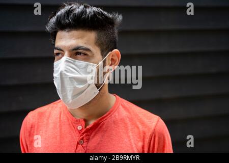 Giovane arabo con una maschera protettiva nel mezzo della strada di fronte a un muro di legno blu Foto Stock