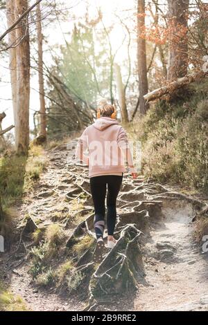 Vista posteriore di una donna sportiva attiva che ascolta la musica mentre corre nella foresta autunnale. Allenamento femminile all'aperto. Un'immagine sana dello stile di vita Foto Stock