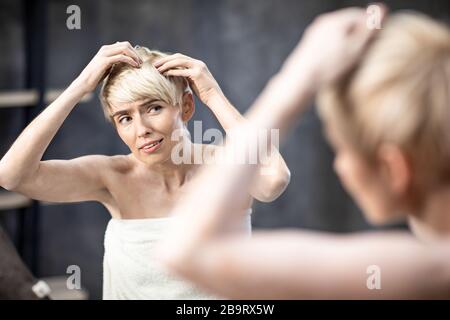 Lady sofferenza da Dandruff problema toccando capelli in piedi a casa Foto Stock