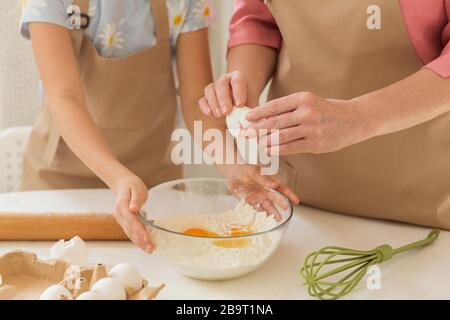 Cucina familiare. Signora Maure aggiungendo uovo alla farina mentre la bambina che la aiuta in cucina, closeup Foto Stock