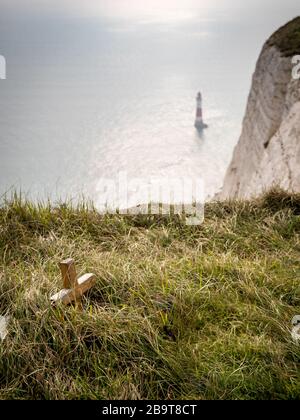 Beachy Head, faro e memoriale. Focus su un piccolo crocifisso di legno posto in memoria di qualcuno che è caduto vittima del famigerato luogo suicida. Foto Stock