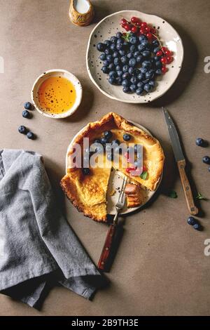 Iniziato mangiati freschi di forno olandese pancake bambino nella piastra ceramica servita con blackberry e rosse bacche Ribes, ciotola di miele, brocca di crema, taglio vintage Foto Stock