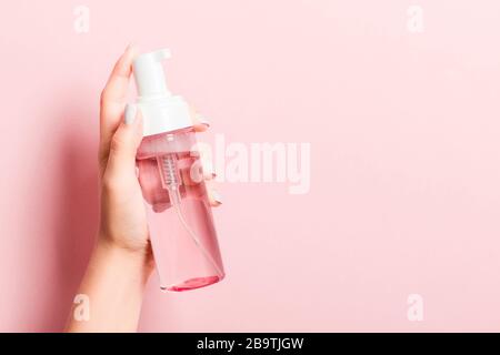 La mano della donna sta tenendo uno spray cosmetico a sfondo rosa con spazio di copia per il vostro disegno. Foto Stock