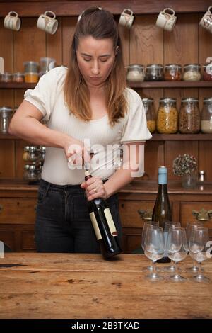Una degustazione di vino femminile che apre una bottiglia di vino rosso Foto Stock