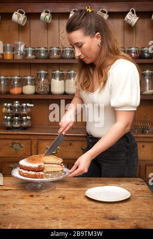 Una donna che taglia una fetta di torta fatta in casa Victoria Sponge Foto Stock