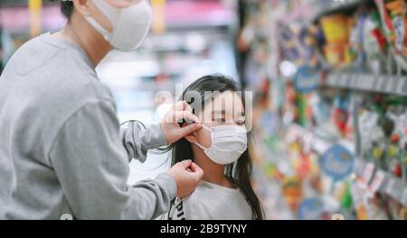 La madre che indossa una maschera protettiva mette una maschera facciale su una figlia nel supermercato. Sicurezza durante l'epidemia di COVID-19. Epidemia di virus covid, Foto Stock