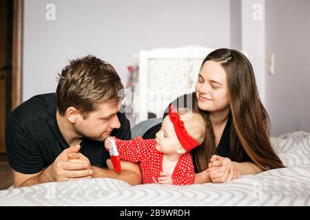 Mamma, papà e neonato giocano a casa. Abiti rossi. Il concetto di famiglia, amore, assistenza all'infanzia e casa. Foto Stock