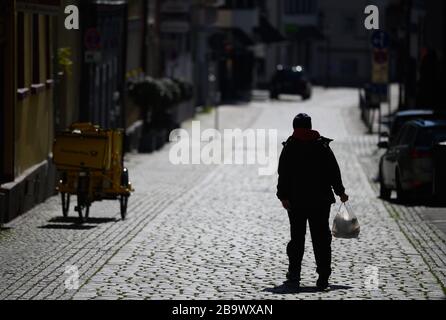 25 marzo 2020, Baden-Wuerttemberg, Eßlingen: Un uomo cammina attraverso una strada vuota nel centro della città con una borsa contenente cibo da asporto. Nel tentativo di rallentare la diffusione del coronavirus, la vita pubblica è stata in gran parte ridotta. Foto: Sebastian Gollnow/dpa Foto Stock