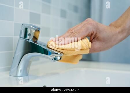 primo piano di un uomo caucasico che pulisce il rubinetto di un lavandino con un panno in microfibra Foto Stock