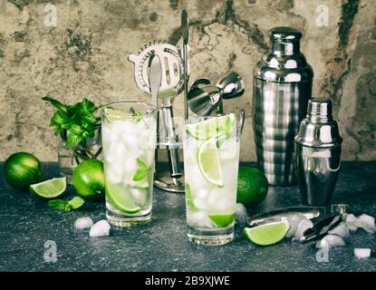 Cocktail Mojito con lime e menta in vetro su un tavolo di pietra. La barra strumenti e ingredienti per cocktail. Foto Stock