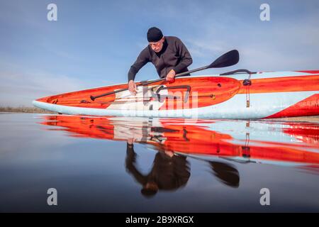 Il paddler maschile senior in una muta sta sciacquando una paddleboard stand up dopo l'allenamento paddling su un lago in Colorado, vista della telecamera d'azione a basso angolo, recrea Foto Stock