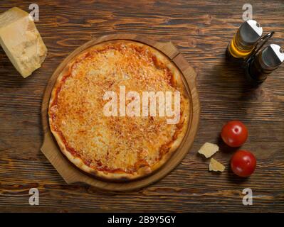 Pizza su un vassoio di legno, pomodori, formaggio, olio d'oliva in un decanter di vetro su un tavolo di legno Foto Stock