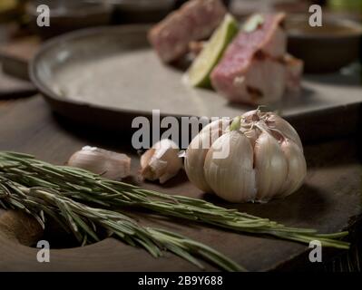 Rosmarino e aglio, gli ingredienti si trovano su un tagliere su uno sfondo di un piatto con bistecca di tonno e lime Foto Stock