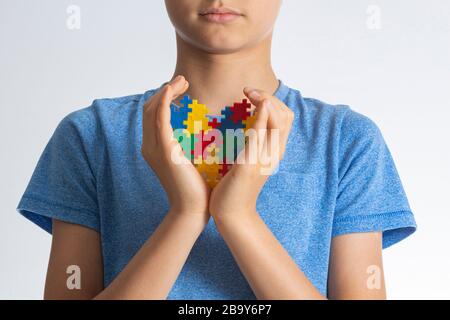 Concetto del giorno di consapevolezza di autismo del mondo. Le mani del bambino tengono il cuore colorato del puzzle contro di lui Foto Stock