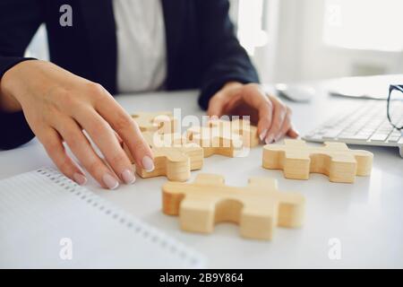 Mani senza volto di una donna d'affari con puzzle di legno su un tavolo bianco in Office.with finestre. Analisi della strategia del team di pianificazione soluzione di idea conce Foto Stock