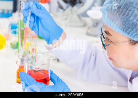 Alla scoperta di una cura per una scienziata asiatica che è concentrata, tenendo una provetta e guardando durante il lavoro. Foto Stock