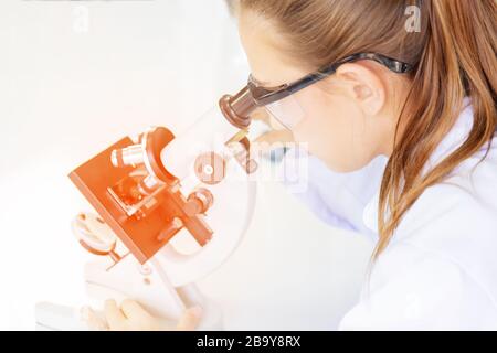Belle donne scienziati stanno guardando i microscopi in un laboratorio di scienza con varie attrezzature in laboratorio e hanno una luce arancione. Foto Stock