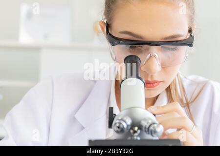 Belle scienziati femminili stanno guardando i microscopi in un laboratorio di scienza con varie attrezzature in laboratorio. Foto Stock