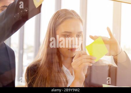 Due uomini e donne d'affari che attaccano le note sul vetro trasparente Foto Stock