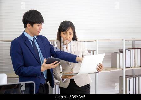 Due giovani uomini d'affari asiatici si incontrano in ufficio in mano al tablet. Foto Stock