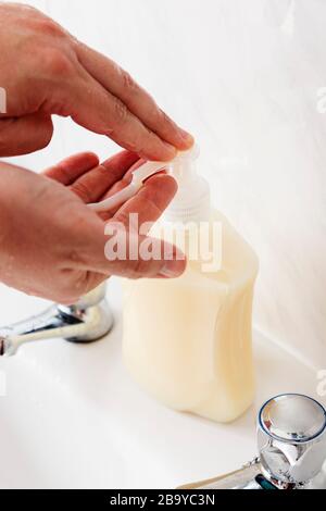 Mano degli uomini prendere il sapone liquido da una bottiglia di sapone, per lavare le mani. Foto Stock