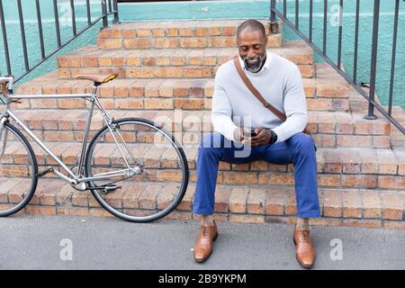 Uomo afro-americano seduto sulle scale e usando il suo telefono Foto Stock