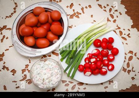 Tradizionale colazione di Pasqua, un mazzo di uova di pollo lesse dipinte con cipolle giovani, ravanelli e insalata francese sul tavolo. Foto Stock