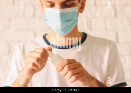 Ritratto di giovane malato con naso che cola con spray nasale. Medico sicuro dell'uomo malato nella maschera medica che tiene le gocce del naso per il naso congestionato. Panoramica Foto Stock